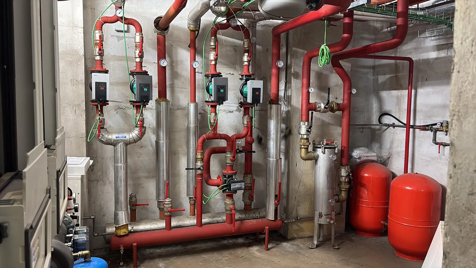 Industrial room with red pipes, multiple pressure gauges, valves, and two large red cylindrical tanks.